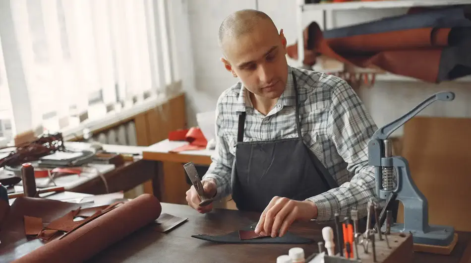 Artisan à l'œuvre sur sa table dans son atelier, travaille une pièce de cuir